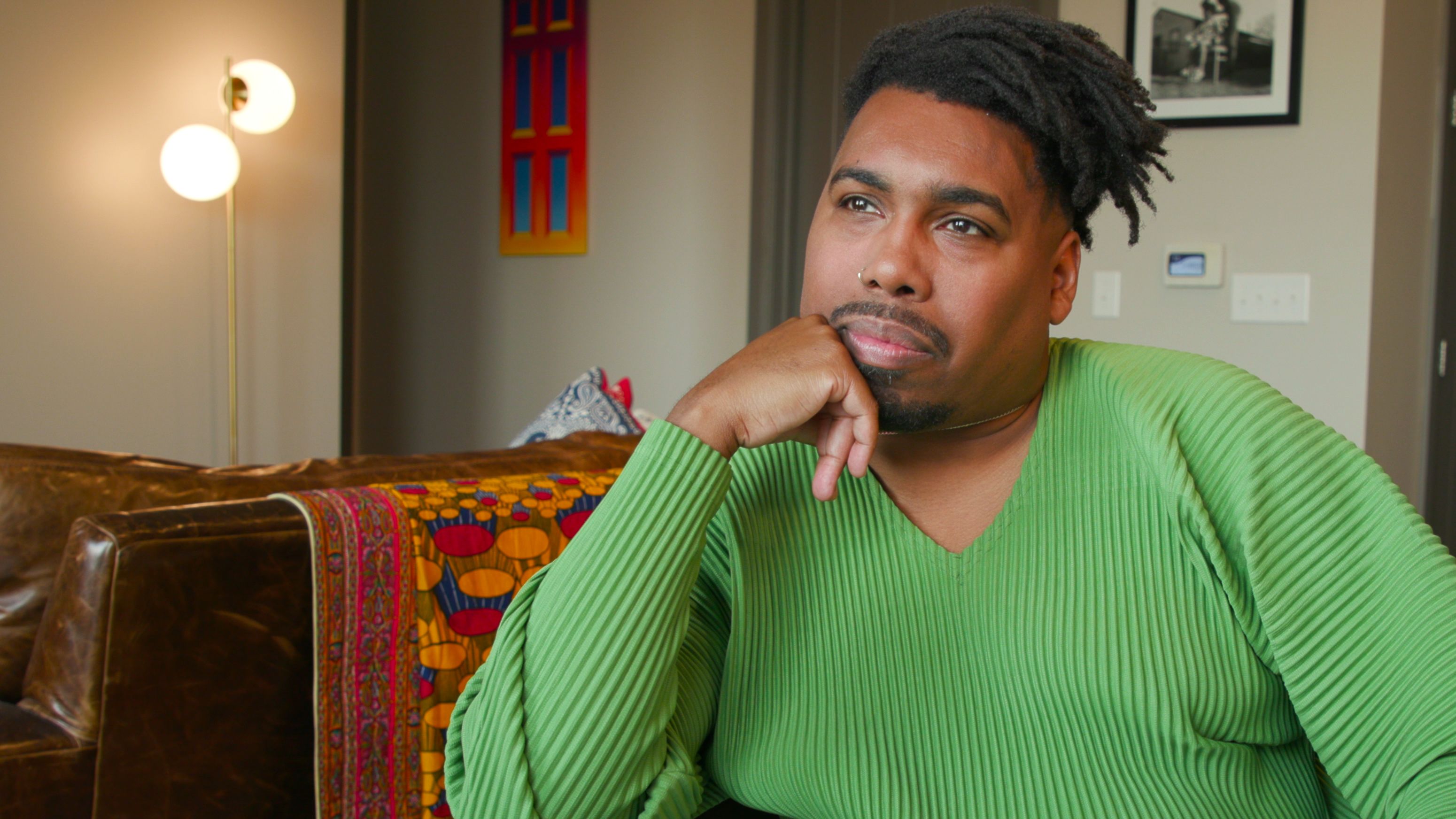 A Black man in a green sweater rests his chin on his hand.