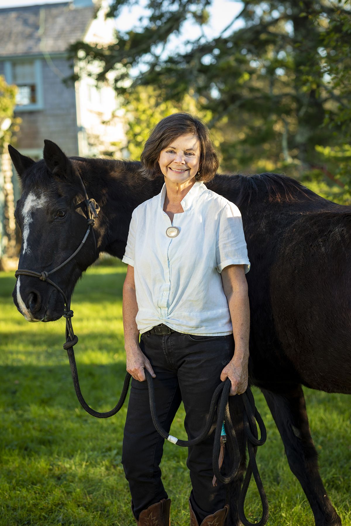Geraldine Brooks stands holding the reins of a horse standing behind her.