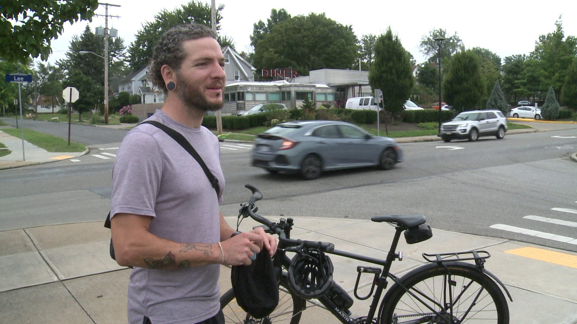 Bicyclist Ernest Durbin stands with his bicycle at the busy intersection where he was hit by a car in 2018.