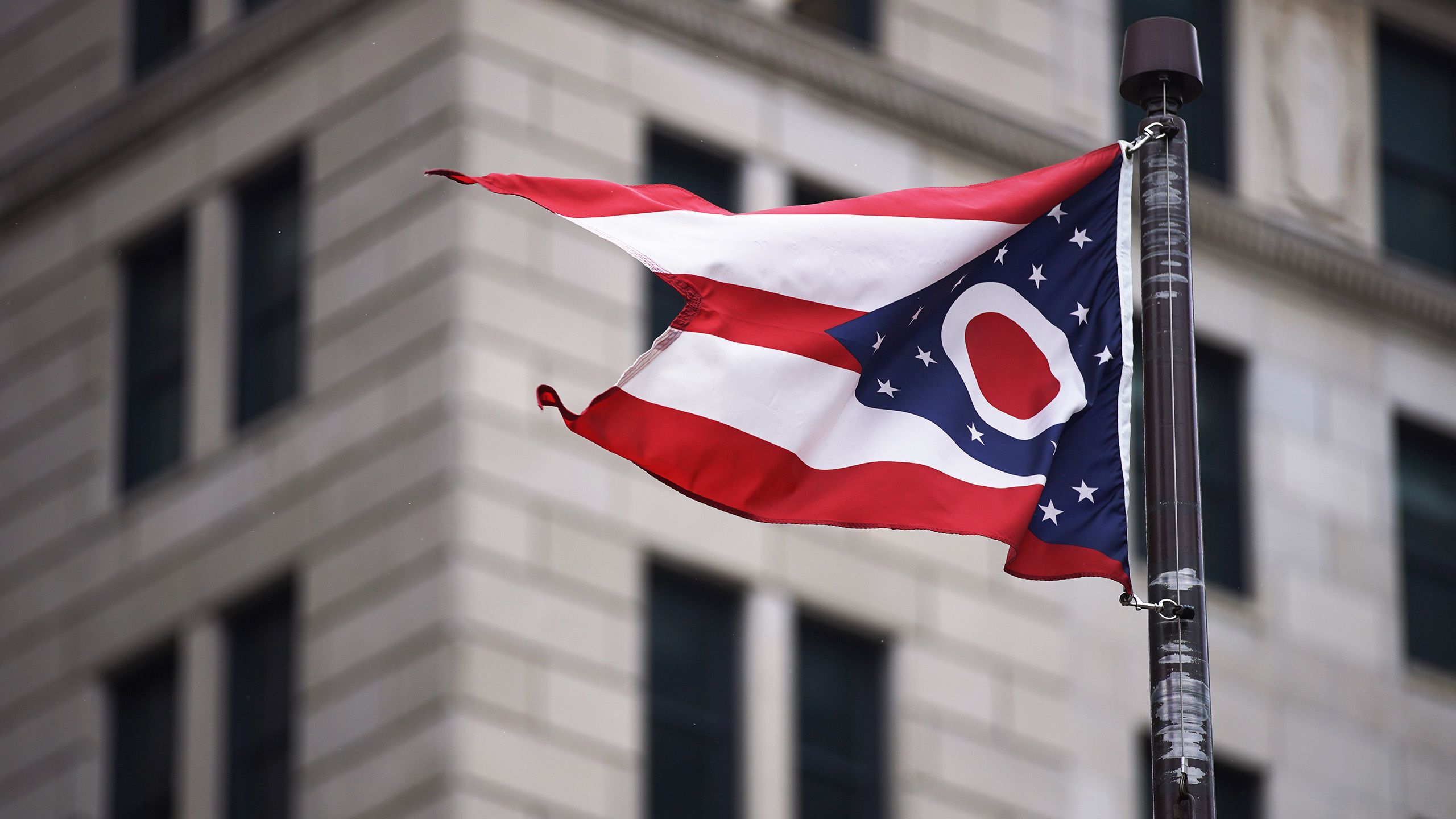 The flag of the state of Ohio waving on a flagpole outside a building in Columbus.