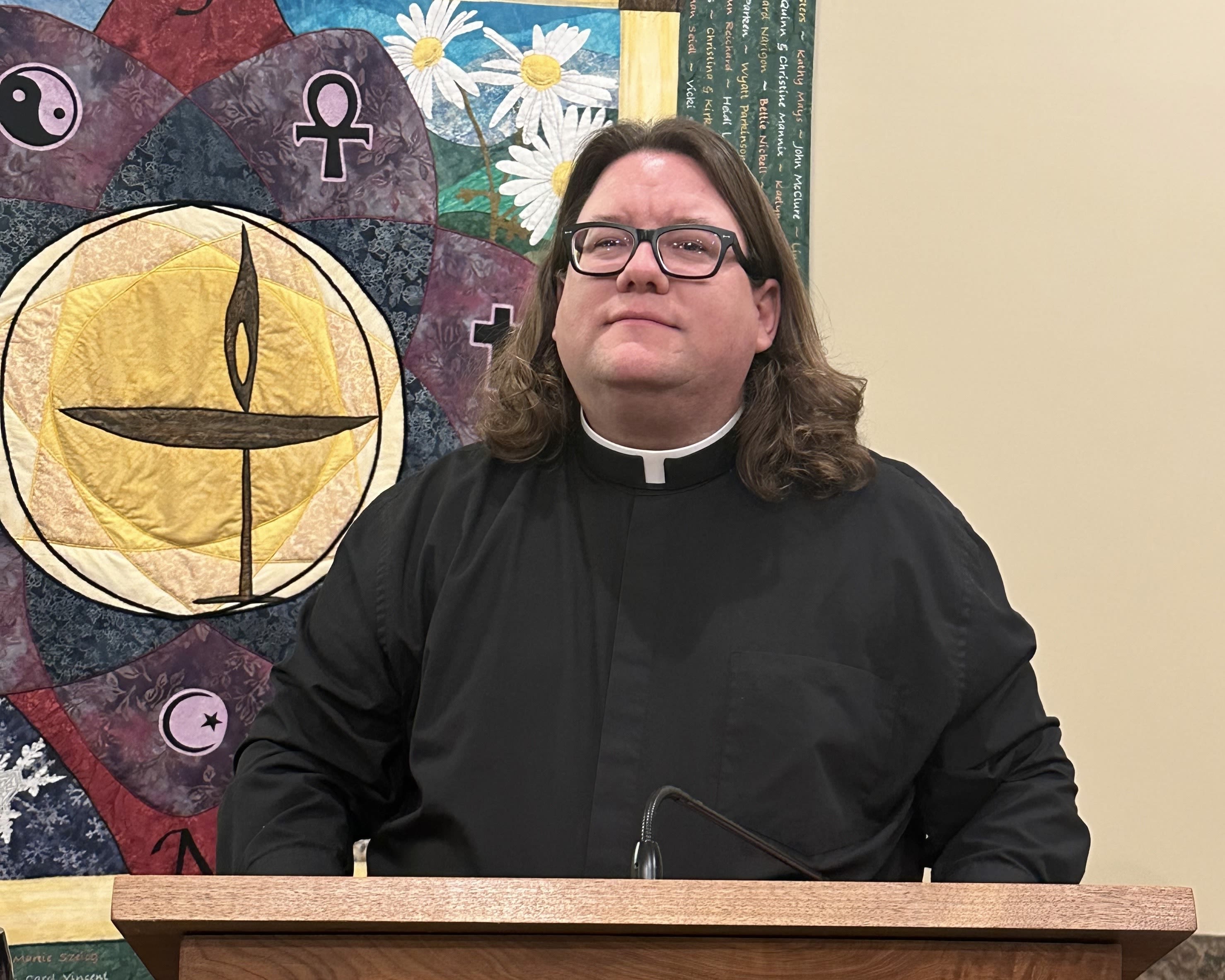 Rev. Terry Williams stands behind his pulpit in front of a hanging quilt.