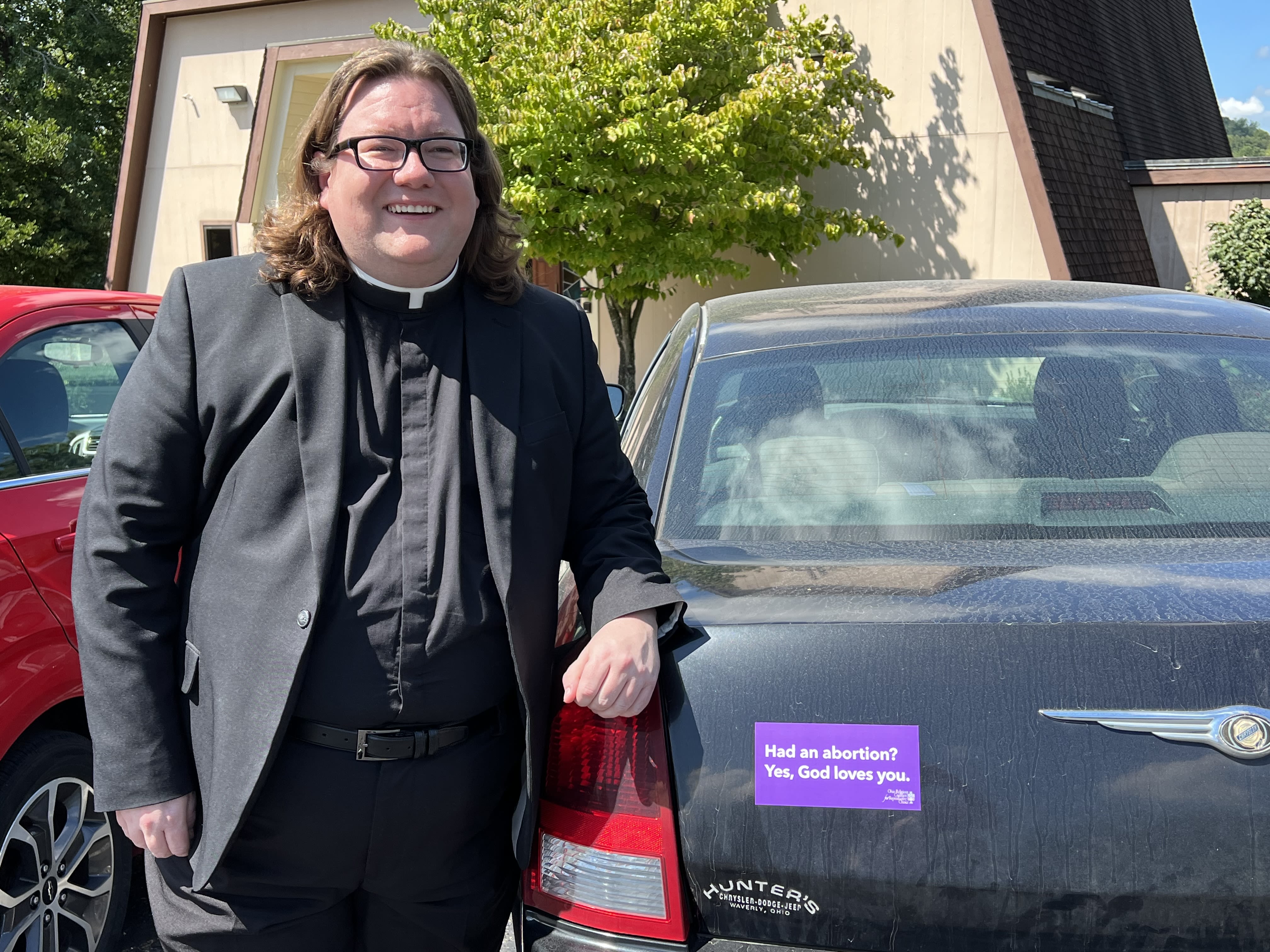 The Rev. Terry Williams, pastor of Orchard Hill United Church of Christ in Chillicothe, stands near the rear end of his car, where he’s placed a purple bumper sticker that reads, “Had an abortion? Yes, God loves you.”