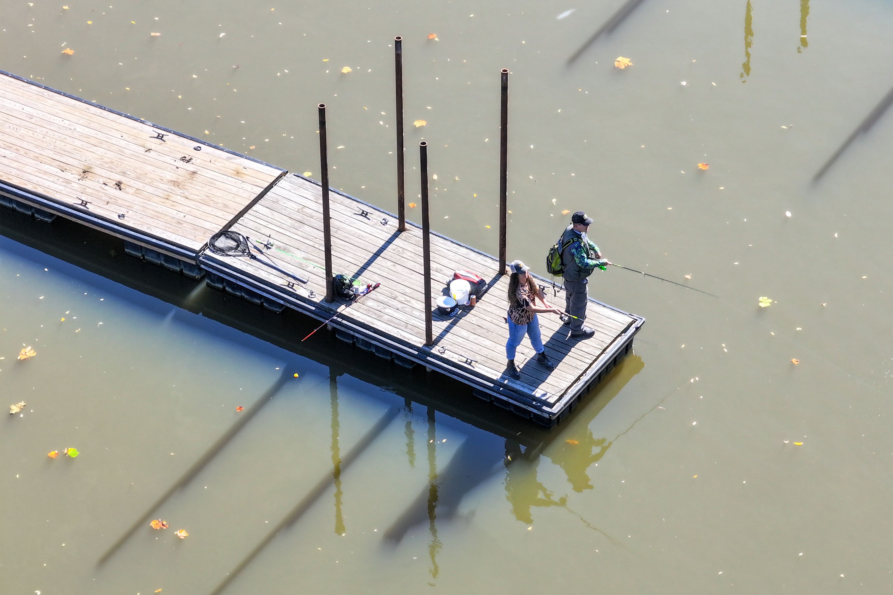Two people stand fishing on a narrow wooden dock.