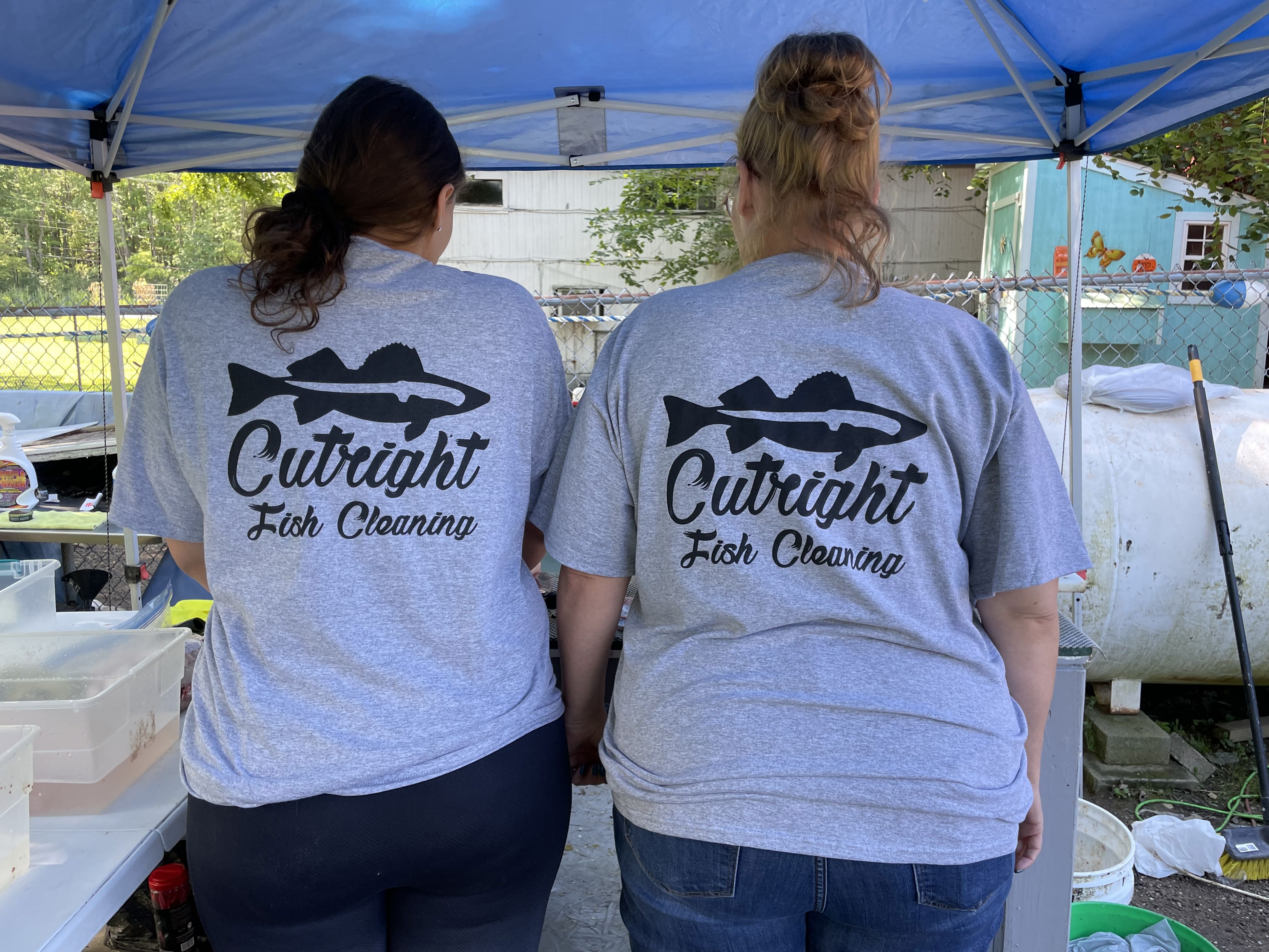 On the back of the shirts of two women, a fish logo is above the name Cutright Fish Cleaning.