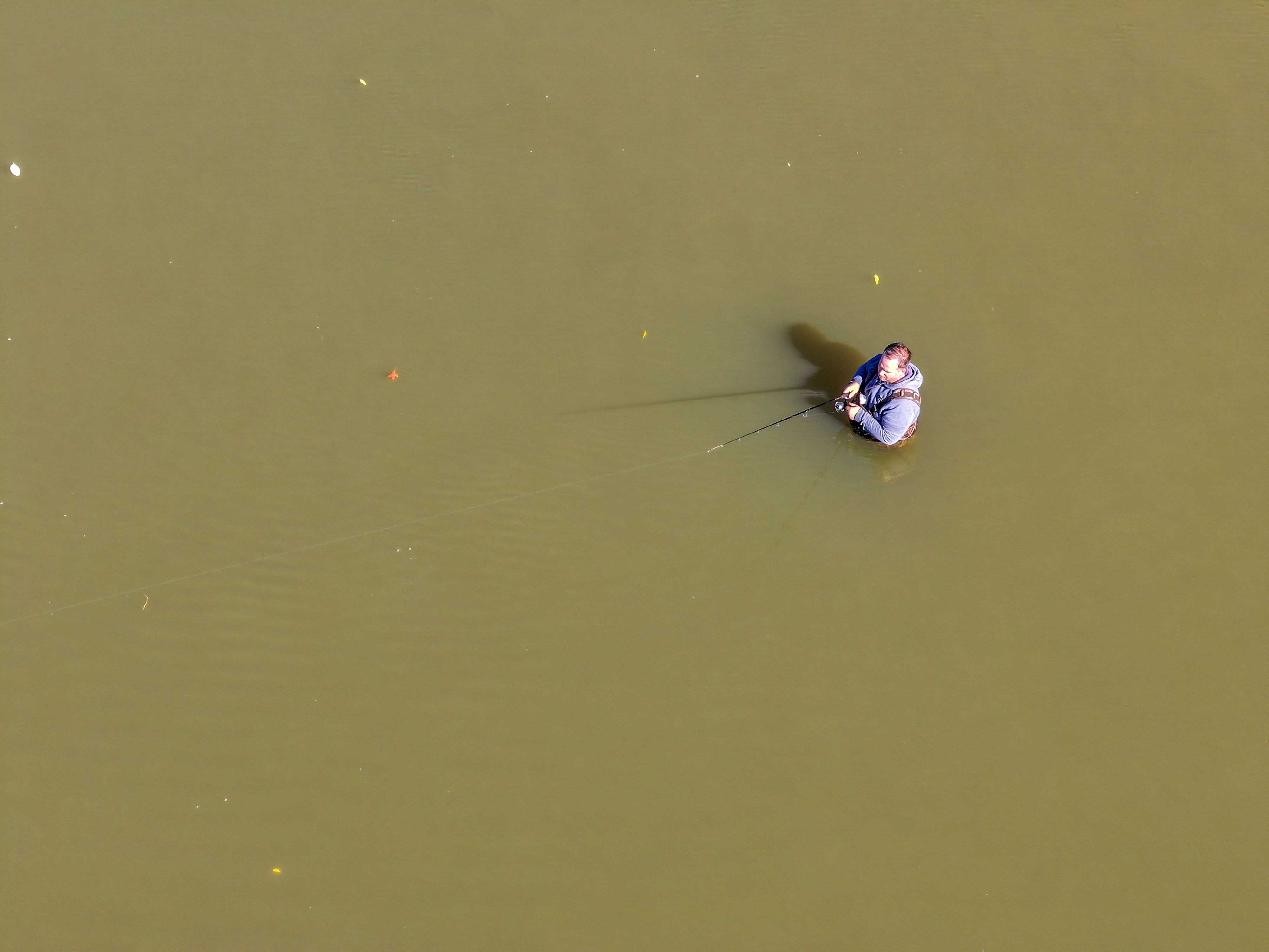 A man stands waist high fishing in a river.