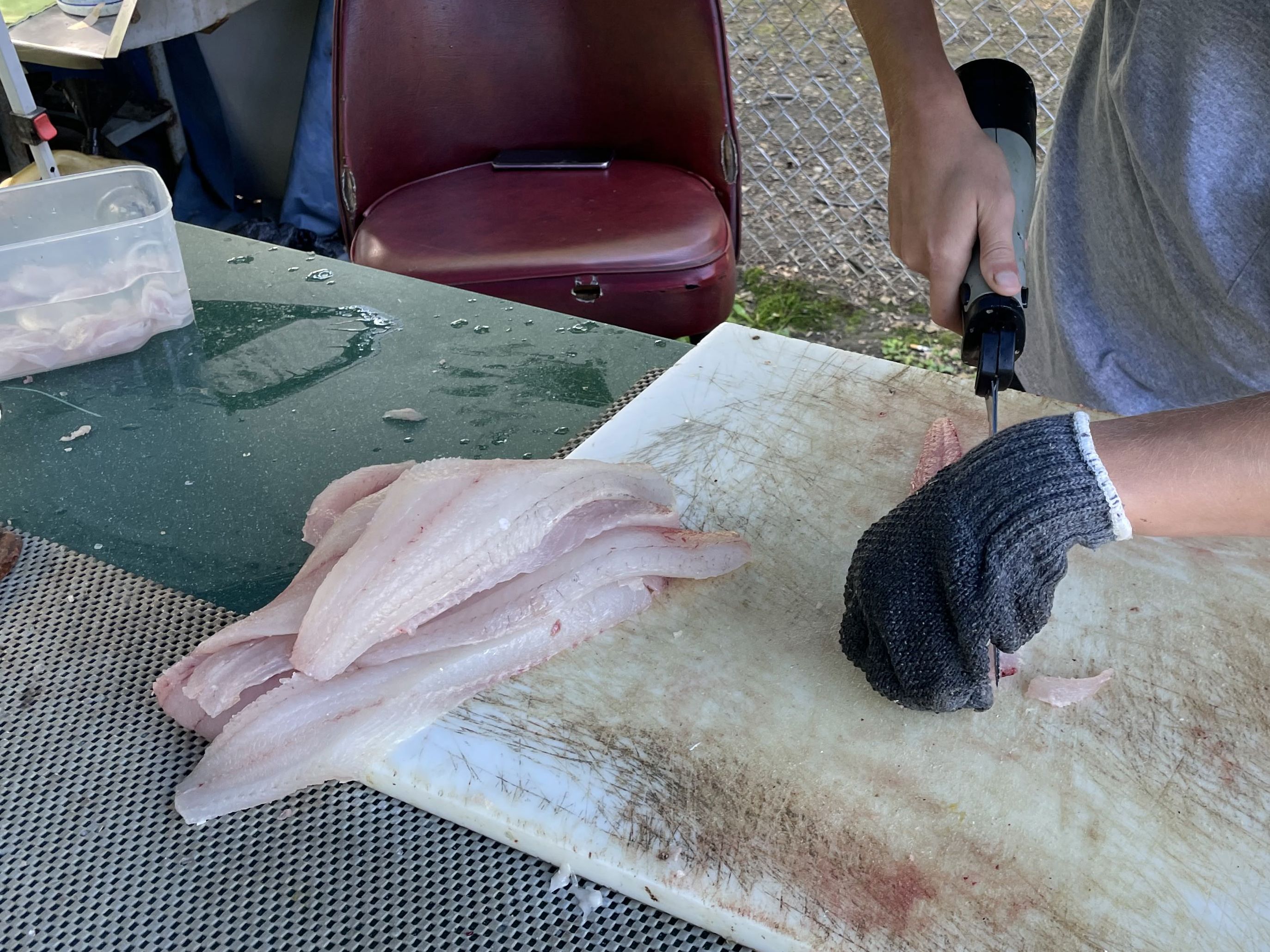 Fillets of walleye n a cutting board where a man is using an electric knife to cut fish.