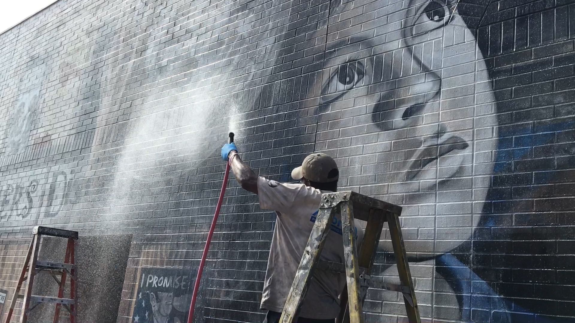 Workers spray down Rivera-Resto' "It's Up to Us" mural as a part of the restoration.