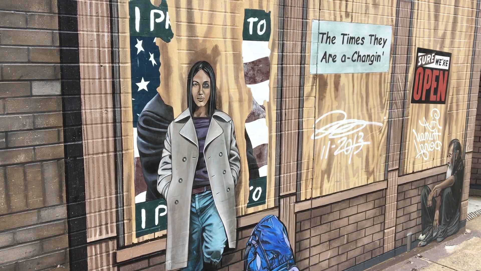 A detail from "It's Up to Us" depicts a young woman with a black eye leaning against a boarded-up storefront in front of a torn political poster.